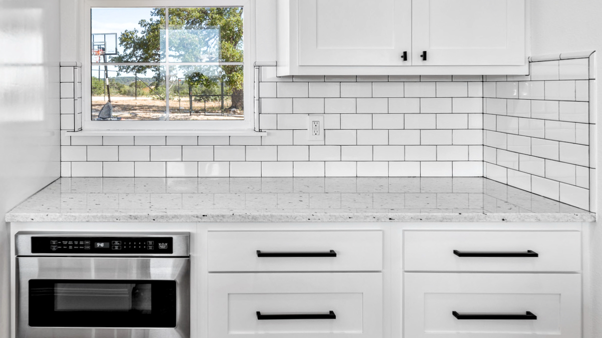 Kitchen with white cabinets with white colored granite containing black dots surrounded white tile on sides