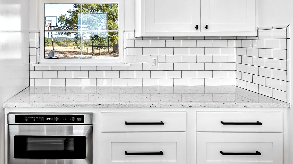 Kitchen with white cabinets and white granite countertops containing black dots, surrounded by white tile